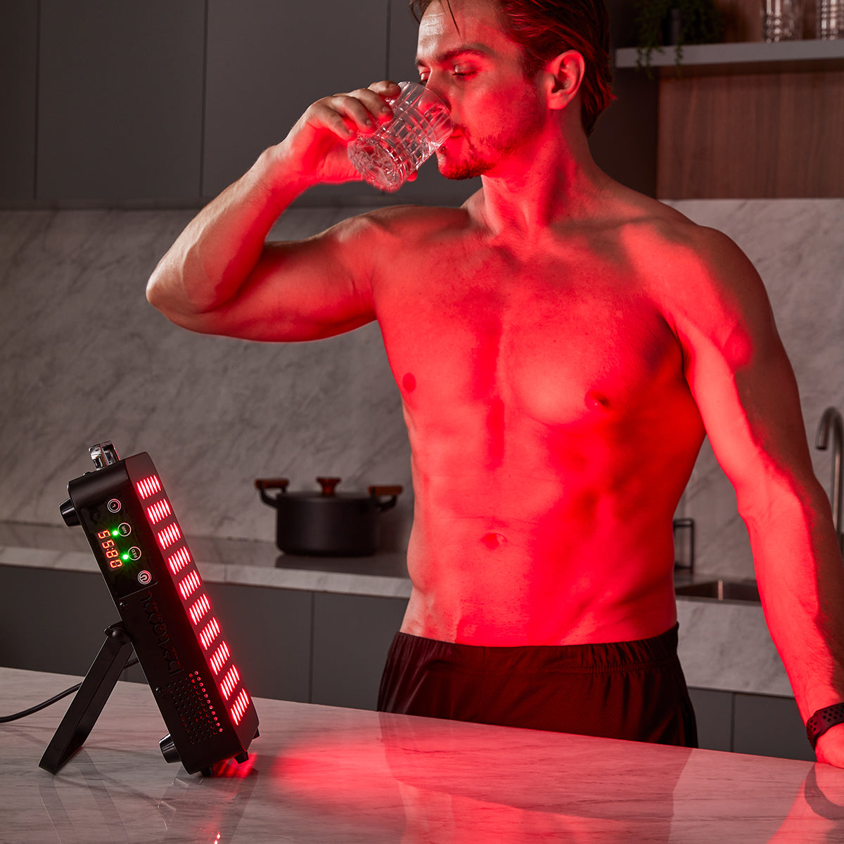 Man using BestQool BQ60 red light therapy panel for at-home wellness, featuring glowing LEDs and digital timer.