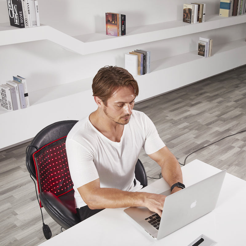 Man working on laptop with BestQool Redot M red light therapy wrap active on his office chair.