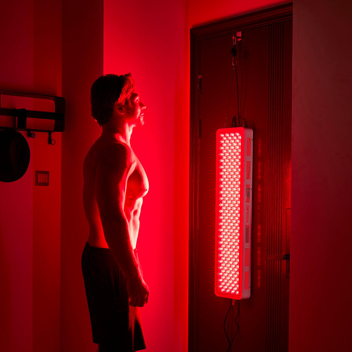 Muscular man using BestQool Pro200 red light therapy panel for at-home wellness and recovery.