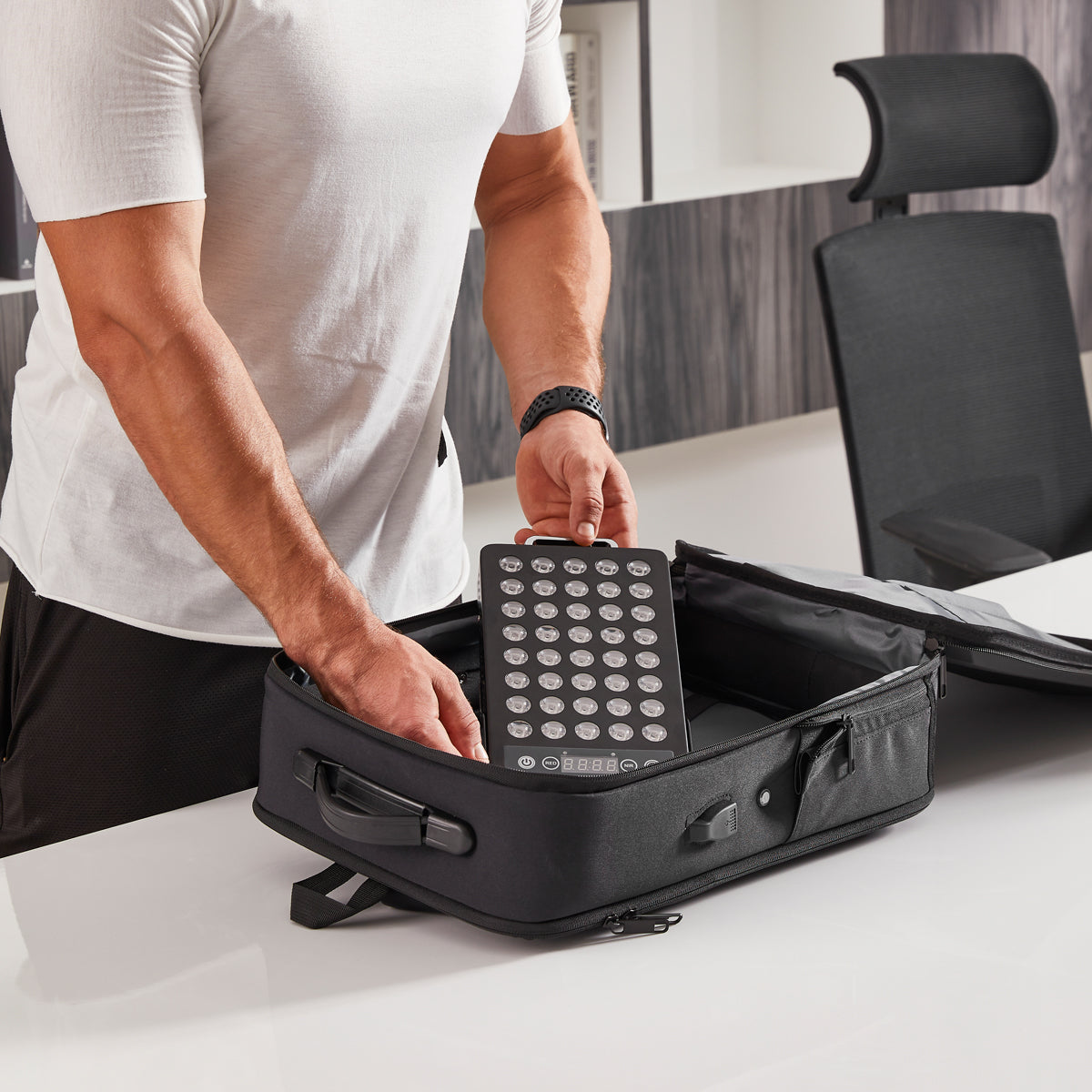 Man placing a black BestQool BQ40 portable red light therapy panel, with 40 LEDs and digital display, into its travel case.