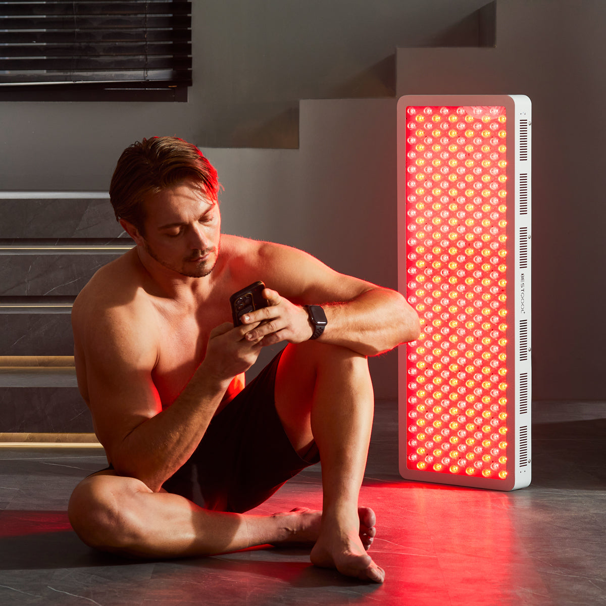 Man relaxing on a mat with a glowing white Bestqool Pro300 full-body red light therapy panel for wellness.